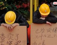2012年12月25日，廣東中山，火炬開(kāi)發(fā)區(qū)的多名建筑工人討要工作一年多的血汗錢一籌莫展，一些工人干脆將鋪蓋卷搬到了售樓部，并在門口搭起灶臺(tái)煮飯，希望以這種方式討回工錢。圖為在銷售中心門外，工人舉牌討薪。吳進(jìn)/視覺(jué)中國(guó)